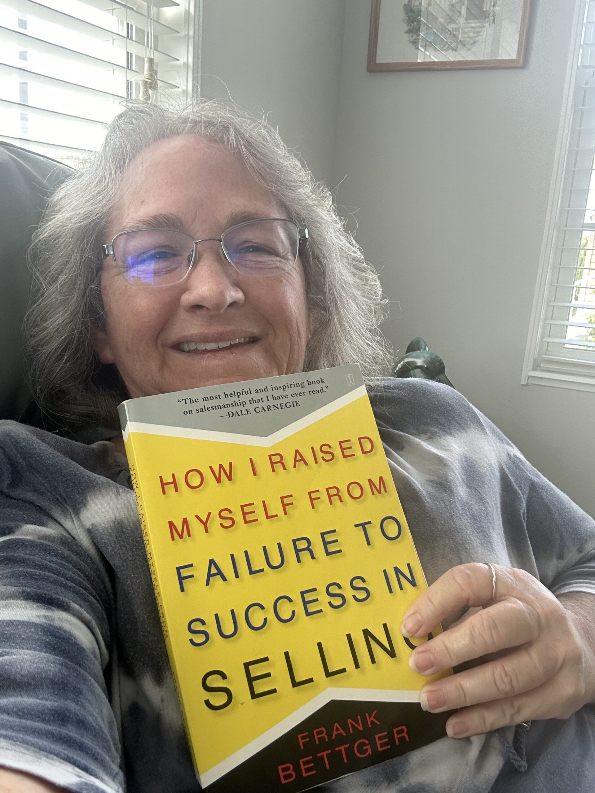 Amy smiling holding How I Raised Myself From Failure to Success In Selling by Frank Bettger.